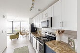 Located at 50-54 Sussex Avenue in Newark, NJ, this modern two-bedroom, two-bathroom residence offers a well-designed open-concept layout across a single floor. The galley-style kitchen is a standout feature, outfitted with white shaker cabinetry, navy blue lower cabinets, granite countertops, a white subway tile backsplash, and stainless steel appliances, including an electric range, microwave, and refrigerator. A stylish pendant track lighting fixture adds a contemporary touch overhead. The kitchen flows seamlessly into the living and dining area, where floor-to-ceiling windows with black frames flood the space with natural light and frame sweeping views of the Newark skyline. Light wood-style flooring runs throughout the main living areas, enhancing the bright, airy atmosphere. The spacious primary bedroom features its own dramatic wall of floor-to-ceiling windows offering city vistas, along with wood-style tile flooring and a walk-in closet. The second bedroom is equally light-filled with large windows and light hardwood-style floors. Both bathrooms are finished with granite-topped white vanities, large-format slate tile flooring, and marble-style tiled shower surrounds. A hallway with a double-door closet connects the living spaces efficiently, completing this polished urban residence.