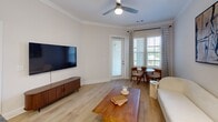 Located at 2200 Pooler Parkway in Pooler, Georgia, this 1-bedroom, 1-bathroom residence offers a cohesive and modern living experience across a single, efficiently designed floor. The welcoming entrance opens into a bright living room finished with light hardwood-style flooring, crown molding, and a ceiling fan. Large windows with stylish grid-patterned curtains invite natural light while offering outdoor views, and a glass door provides direct exterior access. The kitchen is a standout feature, showcasing dark granite countertops, a large undermount sink, stainless steel appliances, and a two-tone cabinet design combining white upper cabinetry with warm wood lower cabinets, complemented by a classic tile backsplash and pendant lighting. The spacious bedroom features crown molding, a ceiling fan, and generous natural light, and connects directly to a well-sized walk-in closet outfitted with wire shelving systems and hardwood-style flooring for practical storage. The bathroom is clean and functional, offering a wood-toned vanity with white countertops, a glass-enclosed shower, and light tile flooring. Neutral tones and consistent finishes throughout the space create a calm, cohesive ambiance suited for comfortable everyday living.