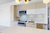 Located on the seventh floor at 1401 S St NW in Washington, DC's vibrant U Street corridor, this thoughtfully designed studio offers an efficient yet refined living experience. The open-plan layout seamlessly integrates the living, dining, and kitchen areas into a single cohesive space. The contemporary kitchen is a standout, featuring two-tone gray and white cabinetry, a glass tile backsplash, stainless steel appliances including a built-in microwave and electric range, and a sleek white-topped island with bar seating beneath a striking globe pendant chandelier. Wide-plank hardwood flooring runs throughout, lending warmth and continuity. Floor-to-ceiling windows in the living and sleeping area flood the space with natural light and frame sweeping views of the Washington, DC skyline, including a notable landmark dome on the horizon. The full bathroom is finished with large-format neutral tiles, a floating vanity with under-cabinet storage, a large mirror, and a glass-enclosed shower. Two dedicated closets provide generous storage, including a built-out walk-in with shelving and hanging space. An in-unit laundry area and a welcoming entrance hall complete the layout, making this a highly functional and stylish urban residence.