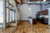 Located at 804 Broadway Blvd in the heart of Kansas City, this single-floor urban loft masterfully combines industrial heritage with modern finishes. The open-concept layout is anchored by rich, original hardwood floors that carry character and warmth throughout the entire space. Soaring ceilings with exposed wood beam detailing and prominent silver ductwork reinforce the loft's industrial aesthetic, while pendant lighting adds a refined touch overhead.

The kitchen is a standout feature, outfitted with dark espresso cabinetry, granite countertops, stainless steel appliances — including a refrigerator, range, and built-in microwave — and a peninsula that opens seamlessly to the main living area. The kitchen's generous vertical space allows upper cabinetry to extend dramatically toward the ceiling, maximizing storage.

Large windows with horizontal blinds fill the space with natural light and frame views of the surrounding Kansas City urban streetscape. Glass-paneled interior doors add an architectural detail that maintains an open, airy feel while defining distinct zones within the loft.

The bathroom features a sleek, modern design with floor-to-ceiling gray tile, a glass-enclosed walk-in shower, a white undermount vanity with dark cabinetry, and consistent hardwood flooring that ties the room to the rest of the space. The overall ambiance is bold, open, and urban.