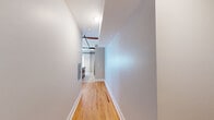Located at 719 Lynn St in Louisville, KY, this 1-bedroom, 2-bathroom unit offers a thoughtfully designed layout with a blend of modern finishes and industrial character. Warm hardwood floors run throughout the living spaces, complementing the neutral gray walls and clean white trim. The entrance hallway leads into an open-concept kitchen and living area, where exposed ductwork and black metal piping lend an industrial aesthetic. The kitchen is a standout feature, boasting rich wood cabinetry, a granite-topped island with a stainless steel sink, pendant lighting, and a full suite of stainless steel appliances including a refrigerator, range, and microwave. The living area is bathed in natural light through multiple large windows with views of the surrounding neighborhood. Ceiling fans are present in both the living area and bedroom. The spacious bedroom features hardwood floors, windows offering outdoor views, and direct access to additional rooms. Two bathrooms serve the unit, one featuring a classic subway-tiled tub and shower surround with wood flooring and chrome fixtures. A dedicated closet and entrance area complete the functional floor plan, making this a well-appointed urban residence.