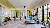 Located at 5150 Adairview Cir in Alpharetta, GA, this fitness center is thoughtfully designed to support a wide range of workout routines across two distinct areas. The main workout room features herringbone-patterned carpet flooring, accent walls in a fresh sage green, and a large mirrored wall that amplifies the sense of space. Recessed lighting and a sleek ceiling fan keep the environment bright and comfortable. Equipment includes a Matrix treadmill, stationary bike, cable machine, free weights with a dumbbell rack, adjustable benches, and an assortment of medicine and stability balls. Large black-framed windows and glass doors flood the space with natural light and offer views of the lush outdoor greenery, with direct access to an exterior patio area. The adjoining studio room offers a clean, open layout with smooth flooring ideal for yoga, barre, or group fitness classes. This room is lined with floor-to-ceiling mirrored walls, a ballet barre, and a wide bank of black-framed windows overlooking manicured grounds. Accent lighting traces the ceiling perimeter, while a ceiling fan and cassette-style HVAC unit ensure year-round comfort. A sliding barn door connects the two spaces seamlessly, creating a versatile and modern fitness facility.
