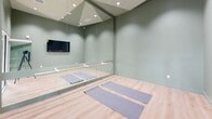 This state-of-the-art fitness facility spans 1420 square feet on a single floor, offering a comprehensive exercise experience. The main exercise room is well-equipped with a variety of modern fitness machines, including treadmills, ellipticals, and weight training equipment. Large mirrors line the walls, enhancing the sense of space and allowing users to monitor their form.

A dedicated yoga studio features a serene atmosphere with sage green walls, recessed lighting, and full-length mirrors. Yoga mats are neatly arranged on the light wooden flooring, ready for use. A mounted TV provides the option for guided sessions.

The facility's design emphasizes natural light, with large windows throughout. A striking feature is the vibrant botanical mural adorning one wall, bringing a touch of nature indoors and creating an energizing atmosphere. The ceiling is equipped with recessed lighting and exposed ductwork, giving the space a contemporary industrial feel.

A spacious hallway connects the different areas, featuring sliding glass doors that lead to the main exercise room. This area also includes amenities such as water stations and informational signage. The overall color scheme of whites, greys, and natural wood tones creates a clean, modern aesthetic that promotes focus and well-being.