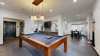 Located at 4000 Essex Lane in Houston's upscale Greenway Plaza neighborhood, this single-floor amenity space is designed to serve as a dynamic hub for socializing, productivity, and relaxation. The open-concept layout is anchored by a central game room featuring a full-size billiard table with a striking pendant light fixture overhead, complemented by a wall-mounted flat-screen TV and a richly detailed wood-paneled bar area, creating an inviting atmosphere for leisure.

Adjacent to the game room, a well-appointed business center provides multiple workstations along a sleek, wall-mounted desk, accompanied by pendant lighting and built-in wood shelving — ideal for remote work or study. The flooring transitions seamlessly between large-format gray tile and rich wood-look tile throughout the space, lending both visual variety and cohesion.

A cozy lounge area offers mid-century modern seating with natural light filtering through wood-slatted blinds, while a separate dining area features a substantial dark wood table surrounded by upholstered teal chairs and generous window views of lush outdoor greenery. A functional kitchenette with stainless steel appliances, a mosaic tile backsplash, and dark wood cabinetry rounds out the space, with restroom access conveniently nearby.