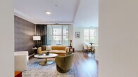 Located in the sought-after Chevy Chase Lake community in Chevy Chase, MD, this thoughtfully designed single-floor residence blends contemporary style with refined comfort. The open-concept living and dining area is bathed in natural light through oversized windows, with rich hardwood flooring flowing throughout. A striking textured accent wall anchors the living space, complemented by tray ceilings and a private balcony accessible through glass doors that frame views of the surrounding neighborhood. The dining area sits adjacent to the living room, creating a seamless, connected layout ideal for both everyday living and entertaining. The kitchen features sage-toned shaker cabinetry extending to the ceiling, stainless steel appliances, a herringbone tile backsplash, and a waterfall-edge quartz island with ample counter space. The primary bedroom offers a bold geometric wallpapered accent wall, large windows with sheer draping, and generous proportions. Its en-suite bathroom includes a walk-in tiled shower, a single-sink vanity with shaker cabinetry, and neutral stone-look flooring. The second bedroom is bright and well-proportioned with large windows and clean finishes. A second full bathroom with a tub-shower combination and a backlit vanity mirror completes the layout.