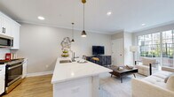 Located at 445 South Ave E in Westfield, NJ, this thoughtfully designed two-story residence offers two bedrooms, two bathrooms, and a generous spread of living space across two floors. The main level is anchored by a bright, open-concept area that seamlessly integrates the kitchen, dining, and living spaces. The kitchen is a standout, showcasing white shaker cabinetry, stainless steel appliances, and a large waterfall-edge quartz island with a built-in sink and pendant lighting overhead. Light hardwood flooring flows throughout the main level, complementing the neutral palette and crown molding details. The living area is filled with natural light from large windows and a sliding glass door that opens onto a private balcony, offering outdoor views of the surrounding community. Upstairs, the primary bedroom provides a comfortable retreat with ample closet space, while the second bedroom features bright windows and plush carpeting. The bathrooms are finished with upscale tile work — one with marble-look flooring and a glass-enclosed shower, the other with floor-to-ceiling tile and a walk-in shower. Additional highlights include in-unit laundry, a utility room, and six closets throughout, ensuring abundant storage across both levels.
