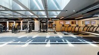 Located in the heart of Miami's vibrant Wynwood arts district, WYND27 is a purpose-built fitness facility offering a comprehensive and well-equipped exercise environment. The single-floor space is defined by its striking architectural ceiling — a large skylight grid that floods the main floor with natural light, creating an open and energizing atmosphere throughout the day. A branded turf sprint track runs the full length of the facility, serving as the central axis around which all equipment is organized, and doubles as a functional training lane for speed and agility work. Along the perimeter and flanking the track, the facility houses an extensive array of strength and conditioning equipment, including cable machines, multi-functional rigs, plate-loaded machines, selectorized weight stations, treadmills, stationary bikes, adjustable benches, and a full dumbbell rack. A dedicated functional training zone features a punching bag, medicine balls, kettlebells, resistance bands, and a large tire for dynamic training. Full-length mirrored walls in select areas enhance the sense of space and allow for form monitoring during workouts. The flooring transitions between rubberized gym surfaces and turf, providing appropriate traction for varied exercises. Linear LED lighting complements the natural daylight, ensuring consistent illumination throughout. The overall design is modern and industrial, with an aesthetic that reflects the creative energy of the surrounding Wynwood neighborhood.