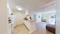 This single-story residence in Concord, California (94521) offers a well-organized, open layout that connects the kitchen and living spaces in a cohesive, functional design. Light wood-style flooring runs throughout, creating a consistent and clean aesthetic across all rooms.

The galley-style kitchen is equipped with white cabinetry, ample drawer and counter storage, a stainless steel sink, and white appliances including a refrigerator and range. A peninsula counter extends toward the living area, providing an informal workspace or dining surface while maintaining an open sightline into the main living space.

The living room is bright and spacious, benefiting from a large sliding glass door that opens to an outdoor balcony and allows generous natural light to fill the room. A wall-mounted unit provides climate control, and the neutral wall tones contribute to the room's airy feel.

The bedroom features a mirrored sliding closet door that reflects light and adds a sense of depth. A window overlooking the balcony further enhances the natural light in this room.

The bathroom includes a single-sink vanity with white cabinetry and light countertops, a tub-shower combination, and matching wood-style flooring. Textured ceilings are present throughout the unit, consistent with the overall design.