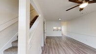 Located at 1301 E Central Ave in Bentonville, Arkansas, this two-story residence offers a clean, functional layout with consistent finishes throughout both levels. The main floor features an open living area with light wood-style luxury vinyl flooring, a ceiling fan, and a staircase leading to the upper level. A pass-through window connects the living space to the kitchen, which is appointed with white shaker-style cabinetry, granite-look countertops, a stainless steel sink, and black appliances including a range and refrigerator. Track lighting and a window with blinds round out the kitchen's practical design. A half bathroom on the main floor includes a granite-topped vanity, wood-style tile flooring, and gold-tone fixtures. Upstairs, the bedrooms are carpeted and bright, each equipped with ceiling fans and windows dressed with horizontal blinds. One bedroom features a walk-in closet with built-in shelving. The full bathroom on the upper level mirrors the home's consistent aesthetic with a granite vanity, white cabinetry, wood-style flooring, and a tub-shower combination. Throughout the home, white walls and neutral tones create a light, cohesive atmosphere.