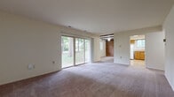 This single-floor residence offers a practical and comfortable layout with well-defined living spaces throughout. The main living area is generously proportioned, featuring neutral-toned carpet and large sliding glass doors that flood the room with natural light and provide direct views of mature trees and a lush green lawn. An adjoining area with exposed beam detailing and a brick accent wall adds a distinct architectural character, creating a warm, informal gathering space.

The kitchen is efficiently designed with warm wood cabinetry providing ample storage, white appliances including a refrigerator, gas range, and dishwasher, and light-toned vinyl flooring. A peninsula counter offers a convenient pass-through and additional workspace.

The bedroom is a quiet, well-proportioned room with plush carpet and a window that brings in natural light. The full bathroom features a wood-toned vanity with a single sink, tiled tub-and-shower combination, a natural light-admitting window, and tile flooring that completes a clean, functional design.

Throughout the residence, neutral wall tones and consistent flooring choices create a cohesive atmosphere, while multiple windows and sliding doors ensure the interior remains bright and connected to the surrounding outdoor environment.