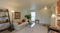 This charming multi-floor property spans three levels, offering a versatile and comfortable living environment. The main living area is bright and welcoming, featuring light-colored carpet flooring that adds warmth underfoot and smooth, neutral-toned walls that create a clean, airy atmosphere. A front entryway opens directly into the living space, allowing for a seamless flow between the entry and the main gathering area. A large window invites abundant natural light, illuminating the room and providing a pleasant connection to the outdoors. The living room is generously proportioned, offering ample space for seating arrangements centered around a glass-top coffee table, while a lean bookshelf along one wall provides functional storage and display space. Decorative touches, including framed artwork and indoor greenery, enhance the overall ambiance with a lived-in, homey feel. A ceiling fan adds practical comfort to the space. With three full floors, this property provides plenty of room for various living, sleeping, and utility needs, making it a highly functional and adaptable home suitable for a range of lifestyles.