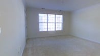 This single-floor space offers a clean, understated aesthetic designed for comfort and versatility. The main room is immediately notable for its generous proportions and bright, welcoming atmosphere. A large, multi-pane window with blinds serves as the focal point of the room, flooding the interior with abundant natural light and creating an open, airy feel. The walls are finished in a crisp, neutral white tone that enhances the sense of space and provides a versatile backdrop for a variety of interior arrangements. Soft, wall-to-wall carpet in a warm beige hue covers the floors, adding a sense of warmth and comfort underfoot. Ceiling-mounted recessed lighting and visible HVAC vents are thoughtfully integrated, ensuring year-round climate control and supplemental illumination. The room's clean lines, neutral color palette, and well-maintained finishes contribute to a bright and composed ambiance throughout. The space presents a move-in-ready environment suited for residential or flexible use, with its simplicity and natural light serving as standout features that make it both functional and inviting.