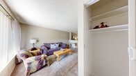 This single-floor unit offers a practical and cohesive layout designed to maximize the use of available space. The living area serves as the central hub, featuring wall-to-wall carpet layered with an area rug, a textured popcorn ceiling, and neutral-toned walls that lend a calm, understated ambiance. A large window fitted with vertical blinds and sheer curtains allows natural light to fill the room, enhancing the open feel of the space.

The living area transitions seamlessly into a compact dining nook, partially separated by a half-wall partition, and then into the kitchen. The kitchen is outfitted with white cabinetry, a white range, refrigerator, and a single-basin sink, all arranged efficiently along one wall. Hard-surface flooring extends through the kitchen and entry areas, providing a practical contrast to the carpeted living zone.

A built-in closet with shelving is accessible near the entryway, offering dedicated storage. The bedroom, visible through the 3D model, is a quiet, contained space with room for furnishings and additional storage. The bathroom features a wide vanity with light countertops, ample under-sink cabinetry, a large mirror, and a shower-tub combination enclosed by a curtain.