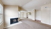 This well-organized single-floor residence offers 2 bedrooms, 2 bathrooms, and a thoughtfully designed layout that maximizes functionality and comfort. The living room serves as the heart of the home, highlighted by soaring vaulted ceilings and a striking corner fireplace with a tile surround. Large windows on multiple walls flood the space with natural light and offer outdoor views, while neutral-toned carpet provides warmth underfoot. The open floor plan connects the living area to a dedicated dining space beneath a classic chandelier, creating a seamless flow throughout. The kitchen features white cabinetry, stainless steel appliances including a refrigerator and electric range, and warm hardwood flooring. Both bathrooms are finished with light countertops, full tub-shower combos with white tile surrounds, and hardwood floors. The bedrooms offer comfortable proportions, plush carpeting, and natural light from exterior windows. Two closets provide ample storage, complemented by a dedicated utility room. The neutral color palette and vaulted ceilings throughout contribute to an airy, open ambiance that makes the space feel generously sized.