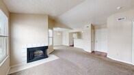 This well-organized single-floor residence offers 2 bedrooms, 2 bathrooms, and a thoughtfully designed layout that maximizes functionality and comfort. The living room serves as the heart of the home, highlighted by soaring vaulted ceilings and a striking corner fireplace with a tile surround. Large windows on multiple walls flood the space with natural light and offer outdoor views, while neutral-toned carpet provides warmth underfoot. The open floor plan connects the living area to a dedicated dining space beneath a classic chandelier, creating a seamless flow throughout. The kitchen features white cabinetry, stainless steel appliances including a refrigerator and electric range, and warm hardwood flooring. Both bathrooms are finished with light countertops, full tub-shower combos with white tile surrounds, and hardwood floors. The bedrooms offer comfortable proportions, plush carpeting, and natural light from exterior windows. Two closets provide ample storage, complemented by a dedicated utility room. The neutral color palette and vaulted ceilings throughout contribute to an airy, open ambiance that makes the space feel generously sized.