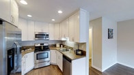 This upstairs unit at 3131 Cauby in San Diego offers a thoughtfully designed single-floor layout with hardwood flooring throughout. The kitchen is a standout feature, showcasing crisp white shaker-style cabinetry that extends to the ceiling, maximizing storage space. Dark granite countertops provide a striking contrast against the white cabinetry, adding a touch of elegance to the space. Stainless steel appliances, including a range with electric cooktop, built-in microwave, and dishwasher, equip the kitchen for everyday functionality. Recessed lighting illuminates the workspace efficiently, while an under-cabinet light above the range enhances visibility during meal preparation. The sink is positioned at the corner of the L-shaped layout, optimizing workflow within the kitchen. The hardwood flooring flows seamlessly from the kitchen into the adjoining hallway and living areas, lending a warm, cohesive aesthetic throughout the unit. Neutral wall tones complement the overall design, creating a clean and inviting atmosphere well-suited to a variety of interior styles.
