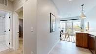This well-appointed single-floor residence showcases a thoughtfully designed open-concept layout that seamlessly connects the kitchen and living areas. Light hardwood-style flooring runs throughout, complementing the crisp white walls and creating a bright, cohesive aesthetic.

The kitchen is a functional centerpiece, featuring warm wood cabinetry with matte black hardware, white quartz countertops, a subway tile backsplash, and a full suite of stainless steel appliances including a range, microwave, dishwasher, and refrigerator. A matte black single-basin sink adds a modern accent. A pendant light fixture anchors the kitchen's transition into the open living space.

The living area is bathed in natural light from a large bank of windows that frame views of the surrounding neighborhood and greenery, creating an inviting and airy atmosphere. A striped area rug adds texture and warmth underfoot.

The bedroom is a calm, well-proportioned retreat finished in soft neutral tones with light wood flooring, offering a serene environment for rest.

The full bathroom is cleanly designed with tile flooring, a wood-framed vanity mirror, white quartz countertop, matte black fixtures, and a tiled tub-shower combination. A welcoming entry hallway with recessed lighting completes this well-planned residence.