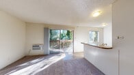 Located at 603 Linden Ln in Martinez, CA, this single-floor unit offers a practical and comfortable layout with well-defined living spaces throughout. The open living area is bright and welcoming, featuring plush carpeting, a textured ceiling, and a wall-mounted air conditioning unit. Large sliding glass doors lead directly to a wooden deck overlooking lush greenery, allowing natural light to fill the room and creating a seamless indoor-outdoor connection. An additional window further enhances the airy feel of the space.

The kitchen is positioned adjacent to the living area, separated by a peninsula counter with a warm-toned laminate surface that doubles as a breakfast bar. White cabinetry lines the walls, providing ample storage, while white appliances — including an electric range with overhead ventilation and a refrigerator — complete the functional cooking space. Wood-look flooring grounds the kitchen area with a durable, easy-to-maintain finish.

The bedroom is a quiet retreat with soft carpeting, a sliding closet, and a window that admits natural light. The bathroom features clean white tile surrounding a full tub and shower combination, accented by a small window for ventilation. Throughout the unit, the neutral color palette and consistent finishes create a cohesive, understated atmosphere.