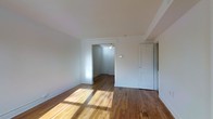 This two-floor space combines classic architectural character with a clean, understated aesthetic. The interior is defined by warm hardwood floors that run throughout, showcasing natural wood tones that add depth and warmth to each room. Crisp white walls provide a bright, neutral backdrop that enhances the sense of openness and allows natural light to reflect generously across the living areas.

The layout features a well-connected flow between rooms, with open doorways that create a sense of continuity from one space to the next. A ceiling fan is visible in the adjoining room, providing both functional air circulation and a traditional design touch. The doorways are framed with classic white trim that complements the overall clean and simple style of the space.

Ample natural light filters through the rooms, casting warm sunlight patterns across the hardwood floors and contributing to an inviting and airy atmosphere. The white walls and doors, paired with the richness of the wood flooring, strike a balance between minimalism and warmth. Storage is also incorporated into the layout, with a built-in closet door visible along one wall. Overall, this space presents a bright, well-maintained, and classically styled interior spread across two floors.