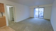 This single-floor unit offers a straightforward, functional layout designed for comfortable everyday living. The living area is generously proportioned, featuring neutral wall-to-wall carpeting and crisp white walls that create a clean, open feel. A large sliding glass door floods the space with natural light and provides views of the surrounding neighborhood. A louvered closet door adds built-in storage conveniently within the living area.

The galley-style kitchen runs efficiently along two parallel walls, featuring warm oak cabinetry that provides ample upper and lower storage. White appliances, including a gas range with overhead ventilation and a full-size refrigerator, are complemented by light wood-toned laminate flooring and a single-basin sink.

The bedrooms are carpeted and bright, each benefiting from windows that draw in natural light and offer outdoor views. One bedroom includes a standard reach-in closet with louvered bifold doors and a hanging rod, while the primary bedroom features a spacious walk-in closet with wraparound shelving and upper storage — a notable organizational asset.

The bathroom maintains a clean, minimal aesthetic with a white vanity, single-basin sink, chrome fixtures, and dual mirrored medicine cabinets above. Throughout, the unit maintains a neutral, move-in-ready palette.