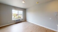 Located on West Lake Street in Minneapolis's Uptown neighborhood, this single-floor unit offers a clean, modern interior designed for functional everyday living. The open layout is finished with light wood-tone flooring throughout, creating a cohesive and bright feel across all living areas.

The main living space is generously proportioned, with neutral gray walls and large sliding windows that invite natural light and offer elevated views of the surrounding neighborhood's tree-lined streetscape. A wall-mounted PTAC unit provides individual climate control. The layout includes an open closet area with built-in shelving and hanging rods, offering organized storage directly accessible from the living space.

The compact kitchen is integrated into the unit, featuring stainless steel appliances including a refrigerator and microwave, white cabinetry, and a subway tile backsplash. A half-wall partition subtly separates the kitchen from the living area while maintaining an open feel.

The bathroom is well-appointed with light tile flooring, a white vanity with ample drawer and cabinet storage, a large framed mirror, and a tall storage cabinet. Overhead lighting illuminates the space effectively. The unit's overall aesthetic is contemporary and clean, suited for urban living in one of Minneapolis's most walkable and active neighborhoods.