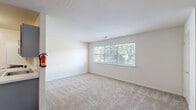 Located at 500 Chews Landing Rd in Lindenwold, NJ, this one-bedroom, one-bathroom unit offers a practical and well-organized layout across a single floor. The space is accessed via a staircase entry, lending a sense of separation and privacy from the outside.

The open living area is finished with neutral-toned wall-to-wall carpeting and features a large multi-pane window that invites natural light and provides pleasant views of the surrounding greenery. A white railing lines the staircase opening, adding a clean architectural detail to the room.

The galley-style kitchen is efficiently designed, featuring gray cabinetry, white countertops, hardwood-style flooring, and stainless appliances including a refrigerator. A washer and dryer are also accommodated within the kitchen area, adding everyday convenience.

The bedroom is generously proportioned, offering ample room for furnishings, and is finished with the same soft carpeting found throughout the living spaces. It benefits from natural light and a dedicated closet for storage.

The bathroom echoes the kitchen's design aesthetic with matching gray cabinetry, a white countertop vanity, hardwood-style flooring, and a full bathtub/shower combination. The clean, white walls throughout the unit create a bright and neutral backdrop ready for personalization.