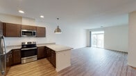 This well-appointed single-floor residence offers a thoughtfully designed open-concept layout that seamlessly connects the kitchen and living area. The kitchen is a standout feature, showcasing rich dark-wood cabinetry, granite countertops, a peninsula with pendant lighting, and a full suite of stainless steel appliances including a refrigerator, range, microwave, and dishwasher. Light wood-style flooring runs throughout the main living areas, lending warmth and continuity to the space.

The expansive living area is bright and airy, with natural light streaming in through large sliding glass doors that open to a private balcony, offering outdoor views of the surrounding neighborhood. The open layout provides generous room for flexible furniture arrangements.

The bedrooms are carpeted for comfort and feature large windows with blinds that allow for ample natural light while maintaining privacy. Each bedroom offers a quiet, restful retreat with generous proportions.

Two bathrooms serve the residence. One features a wide granite-topped vanity with dark cabinetry and a large mirror, while the other includes a sliding glass-door walk-in shower, toilet, and light wood-style flooring. Both bathrooms maintain a clean, modern aesthetic consistent with the rest of the home.