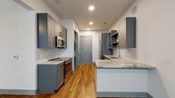 Located at 3233 Harmon Ave in Austin, TX, this efficiently designed single-floor studio offers a thoughtfully utilized layout across a compact footprint. The open-concept kitchen and living area serves as the heart of the space, featuring sleek gray shaker-style cabinetry, marble-look quartz countertops, and a hexagonal tile backsplash. A full suite of stainless steel appliances — including a refrigerator, electric range, built-in microwave, and dishwasher — provides modern functionality. A peninsula counter extends into the living area, offering additional prep space and a natural visual division between the kitchen and living zones. Warm wood-look plank flooring runs throughout the main living areas, complementing the cool gray tones of the cabinetry and walls. The living room benefits from natural light through large windows fitted with horizontal blinds, while a ceiling fan adds comfort. Recessed lighting and open shelving complete the kitchen's contemporary aesthetic. The bathroom features light tile flooring, a marble-look vanity countertop, and direct access to a dedicated closet equipped with multi-level shelving and hanging rods. Clean white walls and consistent finishes throughout create a cohesive, modern ambiance well-suited to Austin's urban lifestyle.