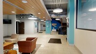This generously sized amenity floor in Syracuse, NY offers a well-rounded collection of resident-focused spaces designed for both relaxation and activity. The entrance areas welcome visitors with large-format white tile flooring, bold teal accent columns, exposed ductwork overhead, and warm wood-paneled ceiling details that lend an urban-industrial character. Pendant lighting and staircase access contribute to an open, connected atmosphere throughout.

The fitness center is a standout feature, spanning a substantial footprint and equipped with a wide array of cardio machines—including treadmills and ellipticals from TRUE Fitness—as well as free weights, resistance equipment, and a stability ball station. Rubber flooring, exposed ceilings, and natural light from street-level windows give the space an energetic, functional feel.

Social and lounge areas are thoughtfully appointed with comfortable seating, wall-mounted televisions, and carpeted flooring in neutral tones. A dedicated coffee bar nook provides a cozy spot for residents to gather, while a game room with a ping-pong table and high-top seating offers casual entertainment. Additional relaxation rooms feature plush sofas, curated artwork, and warm accent lighting. Connecting hallways are wide and well-lit, ensuring easy navigation throughout this comprehensive amenity suite.