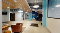 This generously sized amenity floor in Syracuse, NY offers a well-rounded collection of resident-focused spaces designed for both relaxation and activity. The entrance areas welcome visitors with large-format white tile flooring, bold teal accent columns, exposed ductwork overhead, and warm wood-paneled ceiling details that lend an urban-industrial character. Pendant lighting and staircase access contribute to an open, connected atmosphere throughout.

The fitness center is a standout feature, spanning a substantial footprint and equipped with a wide array of cardio machines—including treadmills and ellipticals from TRUE Fitness—as well as free weights, resistance equipment, and a stability ball station. Rubber flooring, exposed ceilings, and natural light from street-level windows give the space an energetic, functional feel.

Social and lounge areas are thoughtfully appointed with comfortable seating, wall-mounted televisions, and carpeted flooring in neutral tones. A dedicated coffee bar nook provides a cozy spot for residents to gather, while a game room with a ping-pong table and high-top seating offers casual entertainment. Additional relaxation rooms feature plush sofas, curated artwork, and warm accent lighting. Connecting hallways are wide and well-lit, ensuring easy navigation throughout this comprehensive amenity suite.