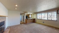 Located in Spokane's South Hill neighborhood, Unit 203 at 1433 West 9th Avenue is a thoughtfully designed single-floor residence that balances comfort and functionality. The open-concept living and dining area is generously proportioned, featuring plush wall-to-wall carpeting, a textured ceiling, and a standout tiled fireplace with a classic wood mantel — an ideal focal point for the main living space. Large windows allow natural light to fill the room, offering views of the surrounding greenery.

The kitchen is efficiently designed with warm wood cabinetry, light countertops, a tiled backsplash, and black appliances including an electric range and an over-the-range microwave. A peninsula with bar-height seating connects the kitchen to the living area, making it a natural hub for entertaining and everyday living.

The bedroom is a comfortable retreat, complete with a ceiling fan, multiple closets including a built-in shelved storage closet, and direct access to the bathroom. The bathroom features wood-toned cabinetry, a tiled vanity backsplash, and speckled vinyl flooring. An additional room provides flexible space suitable for a second bedroom or home office, also featuring a ceiling fan and ample natural light. The unit includes a wall-mounted AC unit and in-unit water heater for added convenience.