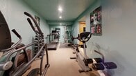 Located at 4440 Beard Ave S in Minneapolis, Minnesota, this dedicated fitness facility offers a compact yet fully functional wellness space across a single floor. The space is divided into two primary exercise areas along with an additional room, providing a comprehensive setup for both cardio training and relaxation.

The main exercise room is finished with soft teal-painted walls and carpeted flooring, creating a practical and energizing environment. It is outfitted with a wide array of fitness equipment, including treadmills, an elliptical trainer, a stationary bike, a multi-station cable weight machine, and a full rack of dumbbells. Wall-mounted workout guides and a large mirror enhance the functional character of the room, while recessed ceiling lighting provides even illumination throughout.

Adjacent to the main gym area is a traditional sauna room that stands out as a notable feature of the space. The interior is fully clad in warm, rich cedar wood planking on the walls, ceiling, and benches, lending it an authentic and inviting character. A classic sauna heater with volcanic rocks sits in the corner, and the floor is finished with white mosaic tiles, adding a clean contrast to the warm wood tones.

Together, these spaces offer a well-rounded fitness experience, combining active workout capabilities with a restorative sauna retreat.