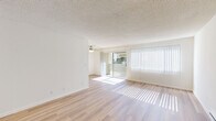 Located at 6184 Cottle Road in San Jose, CA, this single-floor residence offers a well-organized layout with two bedrooms, two bathrooms, a living room, and a kitchen. The spacious living room is bathed in natural light streaming through large vertical-blind windows and a sliding glass door that opens to a balcony, complemented by a ceiling fan and light hardwood-style flooring throughout. A wall-mounted A/C unit and baseboard heating ensure year-round comfort. The kitchen features ample white cabinetry with brushed nickel hardware, generous countertop space with a speckled finish, and matching light wood flooring, providing a clean and functional cooking environment. Both bedrooms are carpeted for warmth and comfort; the primary bedroom offers a sliding closet and a window with outdoor greenery views, while the second bedroom also includes a sliding closet. Each bathroom is finished with white vanity cabinetry, brushed nickel fixtures, and hardwood-style flooring. The full bathroom includes a shower-tub combination, while the second bathroom features a well-lit vanity with a large mirror. Textured ceilings and a neutral white color palette throughout give the home a bright, clean ambiance.