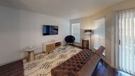 This single-floor residence is designed with a cohesive modern aesthetic, uniting each room through rich hardwood-style flooring and a neutral color palette of warm whites and deep browns. The kitchen is equipped with stainless steel appliances, including a refrigerator, electric range, and over-the-range microwave. Dark espresso-toned cabinetry with sleek hardware is paired with crisp white countertops and a white subway tile backsplash, creating a clean, contemporary contrast. A double-basin sink anchors the counter space, making the kitchen both functional and visually appealing.

The living area offers a comfortable, open layout with multiple windows fitted with horizontal blinds, allowing ample natural light while maintaining privacy. The space easily accommodates a full seating arrangement and wall-mounted television setup.

The bedroom is a well-proportioned retreat featuring large windows on two walls, a ceiling fan with integrated lighting, and the same hardwood-style flooring found throughout the unit. The room receives generous natural light and offers a calm, restful atmosphere.

The bathroom includes a full soaking tub and shower combination with floor-to-ceiling dark tile surround, a curtained rod, a standard toilet, and a separate vanity area with a dark wood cabinet, white countertop, and lighted mirror. A private door adjacent to the tub area adds functional separation within the space.