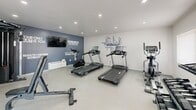 Located at 614 Sheridan Lake Rd in Rapid City, South Dakota, this fitness center offers a clean, modern environment designed to support a well-rounded workout routine. The space is housed on a single floor and is thoughtfully outfitted with a variety of exercise equipment, making efficient use of its compact footprint.

The room features light-toned tile flooring and crisp white walls, creating a bright and energizing atmosphere. Recessed ceiling lighting ensures the space is well-illuminated throughout. A standout design element is the motivational typography wall mural, which reinforces a fitness-focused ambiance, complemented by a dedicated accent wall in deep navy blue featuring an integrated flat-screen television and additional motivational quotes.

Cardio equipment includes multiple treadmills and an elliptical machine, providing ample options for aerobic training. A multi-function cable machine supports a wide range of strength and resistance exercises, while a tiered dumbbell rack with a full set of free weights caters to targeted strength training. A workout bench adds further versatility to the available training options.

Natural light filters in through a window, and a glass-panel door provides direct exterior access. The overall design is minimal and functional, keeping the focus on fitness while maintaining a welcoming, professional atmosphere.