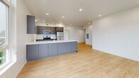 Located at 3956 N Vancouver Ave in Portland, OR, this modern 2-bedroom, 2-bathroom unit offers a well-designed, single-floor layout with a clean, contemporary aesthetic. Light-toned hardwood flooring flows throughout the main living areas and bedrooms, complementing the crisp white walls and recessed lighting that keep the space bright and airy.

The open-concept kitchen is a standout feature, anchored by a generous island with a white quartz countertop, an integrated sink, and sleek gray cabinetry. Stainless steel appliances — including a gas range, microwave, and refrigerator — complete the modern look, while tall windows along the kitchen wall invite abundant natural light and views of surrounding greenery.

Both bedrooms are well-proportioned, each equipped with closet space. The primary bedroom benefits from a large corner window arrangement offering views of the neighboring building's balconies, flooding the room with daylight. The second bedroom also features a closet and connects easily to the main hallway.

The two bathrooms are finished with large-format white tile flooring, dark gray vanity cabinetry, white quartz countertops, and wide illuminated mirrors. A dedicated laundry area adds everyday convenience. The hallway connects all spaces efficiently, maintaining a clean, functional flow throughout this thoughtfully designed Portland residence.