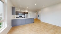 Located at 3956 N Vancouver Ave in Portland, OR, this modern 2-bedroom, 2-bathroom unit offers a well-designed, single-floor layout with a clean, contemporary aesthetic. Light-toned hardwood flooring flows throughout the main living areas and bedrooms, complementing the crisp white walls and recessed lighting that keep the space bright and airy.

The open-concept kitchen is a standout feature, anchored by a generous island with a white quartz countertop, an integrated sink, and sleek gray cabinetry. Stainless steel appliances — including a gas range, microwave, and refrigerator — complete the modern look, while tall windows along the kitchen wall invite abundant natural light and views of surrounding greenery.

Both bedrooms are well-proportioned, each equipped with closet space. The primary bedroom benefits from a large corner window arrangement offering views of the neighboring building's balconies, flooding the room with daylight. The second bedroom also features a closet and connects easily to the main hallway.

The two bathrooms are finished with large-format white tile flooring, dark gray vanity cabinetry, white quartz countertops, and wide illuminated mirrors. A dedicated laundry area adds everyday convenience. The hallway connects all spaces efficiently, maintaining a clean, functional flow throughout this thoughtfully designed Portland residence.
