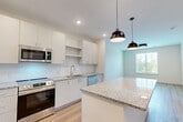 This well-appointed one-bedroom, one-bathroom residence in Peabody, MA offers a thoughtfully designed open-concept layout finished with modern touches throughout. The kitchen serves as the heart of the home, showcasing a large granite-topped island, crisp white cabinetry, a subway tile backsplash, and a full suite of stainless steel appliances including a side-by-side refrigerator, range, built-in microwave, and dishwasher. Stylish black pendant lights hang above the island, complementing the recessed lighting overhead. Light hardwood flooring flows seamlessly throughout the entire residence, lending warmth and continuity. The bedroom is a comfortable retreat featuring a ceiling fan, a window with outdoor views of surrounding greenery, and access to ample closet space. The full bathroom is elegantly appointed with a granite double vanity, a soaking tub, and direct access to a well-organized walk-in closet with built-in shelving and drawers. Additional features include multiple closets for generous storage, a dedicated laundry area, and a clean, neutral color palette that creates a bright and inviting atmosphere throughout the space.