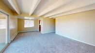 This single-floor, 2-bedroom, 2-bathroom unit is defined by its distinctive exposed ceiling beams and textured ceilings, which add architectural character throughout the living spaces. Warm yellow-toned walls and plush carpeting create a cohesive and comfortable atmosphere across the main living area and bedrooms.

The spacious living room benefits from multiple windows and a large sliding glass door that opens to a balcony with open outdoor views, filling the space with natural light. Baseboard heating runs throughout the unit, providing efficient warmth. A second sliding door in the primary bedroom also offers direct balcony access, complemented by a ceiling fan for added comfort.

The galley-style kitchen is efficiently designed with warm wood cabinetry, granite-look countertops, tile flooring, and a full suite of appliances including a gas range, dishwasher, and refrigerator. A dedicated doorway connects the kitchen to the rest of the unit seamlessly.

Both bathrooms feature tile flooring, wood-framed vanities with granite-look countertops, and natural light from windows. The full bathroom includes a tub-shower combination with tiled surround. The second bedroom offers carpeting and a bright window, maintaining the unit's consistent, comfortable aesthetic.