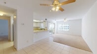 This single-floor residence offers a clean, functional layout bathed in natural light throughout. The open-concept living and dining area is finished with light tile flooring and transitions seamlessly into plush carpeting, creating distinct zones within the shared space. Ceiling fans are installed in both the living and dining areas, contributing to comfortable airflow year-round. Large windows and sliding glass doors connect the interior to the outdoors, filling the space with bright, diffused light and offering views of surrounding greenery.

The kitchen features a pass-through counter that opens directly to the living area, white cabinetry, light-toned countertops, a double stainless steel sink, and a coil-burner electric range. A window above the sink provides additional natural light to the workspace.

The bedrooms are carpeted and well-proportioned, each with ample closet space behind louvered bifold doors. One bedroom includes a sliding glass door leading outside. The bathrooms are straightforward and functional — one includes a tub-shower combination with tile surround, and another features a vanity with a wide mirror and tile flooring. The overall aesthetic throughout the space is light, airy, and neutral, with white walls and bright finishes that create a clean and open atmosphere.