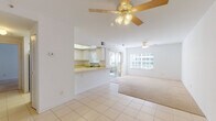 This single-floor residence offers a clean, functional layout bathed in natural light throughout. The open-concept living and dining area is finished with light tile flooring and transitions seamlessly into plush carpeting, creating distinct zones within the shared space. Ceiling fans are installed in both the living and dining areas, contributing to comfortable airflow year-round. Large windows and sliding glass doors connect the interior to the outdoors, filling the space with bright, diffused light and offering views of surrounding greenery.

The kitchen features a pass-through counter that opens directly to the living area, white cabinetry, light-toned countertops, a double stainless steel sink, and a coil-burner electric range. A window above the sink provides additional natural light to the workspace.

The bedrooms are carpeted and well-proportioned, each with ample closet space behind louvered bifold doors. One bedroom includes a sliding glass door leading outside. The bathrooms are straightforward and functional — one includes a tub-shower combination with tile surround, and another features a vanity with a wide mirror and tile flooring. The overall aesthetic throughout the space is light, airy, and neutral, with white walls and bright finishes that create a clean and open atmosphere.