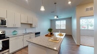 This single-floor space showcases a clean, contemporary design with an open-concept layout that seamlessly connects the kitchen and living areas. The kitchen is a standout feature, equipped with white shaker-style cabinetry, speckled granite countertops, and a full suite of stainless steel appliances, including a refrigerator, range, microwave, and dishwasher. A herringbone tile backsplash adds a refined touch, while a generously sized island with matching granite provides additional prep space and seating. Pendant lighting above the island and recessed ceiling lights ensure the area is well-lit.

Wood-style plank flooring runs throughout the main living areas, contributing warmth and continuity to the space. Ceiling fans are present in multiple rooms, enhancing comfort and airflow. The bedrooms offer plush carpeting and large windows dressed with blinds that invite ample natural light and views of the surrounding area. One bedroom features wood-style flooring in place of carpet.

The bathroom is finished with light wood-tone cabinetry offering generous storage, granite countertops, a vessel sink, and a tiled tub-shower combination. Light tile flooring completes the clean, neutral aesthetic. Overall, the space presents a well-appointed, modern environment with consistent finishes throughout.