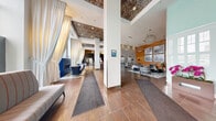 Located at 101 10th St E in downtown Saint Paul, Minnesota, this expansive lobby and hallway space spans over 2,100 square feet on a single floor, offering a striking first impression defined by thoughtful architectural design and upscale finishes. Soaring ceilings with ornate, patterned metallic tile insets lend a sense of grandeur throughout the entry and lounge areas. The main lobby features large-format tile flooring, dramatic floor-to-ceiling windows that flood the space with natural light, and sheer draped curtains that create soft, elegant divisions. A bold reception desk finished in red lacquer with reclaimed wood paneling serves as a focal point, set against a textured mosaic accent wall that rises to full height. The lounge areas are appointed with contemporary furnishings, organic sculptural coffee tables, layered area rugs, and decorative globe pendant lighting. Warm natural wood planking lines several walls, complemented by curated artwork and built-in shelving with a centrally mounted television. Stainless steel elevator doors are framed by the mosaic tile wall, adding a sleek, modern contrast. A dedicated mail room provides rows of individual mailboxes finished in dark bronze, with decorative open shelving above. Together, these spaces convey a refined, welcoming atmosphere suited to a modern residential community.