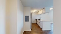 This thoughtfully updated single-floor unit offers a clean, modern aesthetic defined by bright white walls, warm hardwood-style flooring, and an efficient, well-organized layout. The open-concept living area is generously proportioned, allowing for flexible furniture arrangements, and is bathed in natural light through a large window that frames views of the surrounding cityscape.

The galley-style kitchen is well-appointed with white shaker cabinetry, stone-look countertops, a stainless steel refrigerator, stainless steel range, built-in microwave, and dishwasher. Track lighting overhead illuminates the workspace, while the undermount sink with a modern brushed-nickel faucet adds a refined finishing touch. A pass-through counter connects the kitchen to the living area, enhancing the open feel of the space.

The bedroom is a comfortable, light-filled room with the same hardwood-style flooring and a large window offering city views, providing a bright and airy atmosphere.

The bathroom is finished with clean white subway tile, a tub-shower combination with decorative grey tile banding, neutral stone-look floor tile, a white shaker vanity with stone countertop, and a backlit LED mirror, creating a spa-like sense of calm. An electrical panel is conveniently accessible within the unit. Overall, the space presents a cohesive, contemporary interior with quality finishes throughout.