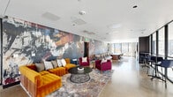 Located in the heart of Denver, CO, this dynamic single-floor commercial space offers a thoughtfully curated environment that blends creative design with functional versatility. The open-plan layout is anchored by a dramatic, large-scale abstract mural that spans an entire wall, infusing the space with bold strokes of color — deep blues, burnt oranges, and rich crimsons — that set a vibrant artistic tone throughout.

Polished concrete flooring runs seamlessly across the entire space, lending an industrial-chic aesthetic that complements the modern furnishings. A lounge area features a plush amber velvet sectional sofa paired with deep magenta armchairs and a round wire-frame coffee table atop a layered area rug, creating an inviting setting for casual meetings or relaxed collaboration.

Adjacent to the lounge, a long wooden conference table with neutral-toned seating provides a more formal meeting environment. A glazed partition wall with slender black steel framing separates a bar-height seating area, where high stools face floor-to-ceiling windows that flood the space with abundant natural light and offer clear views of the surrounding Denver cityscape.

A smaller breakout nook, featuring a marble bistro table and sculptural white chairs set against another mural-covered wall, provides an intimate space for focused conversation. The overall ambiance is sophisticated yet approachable, designed to inspire creativity and productive collaboration.
