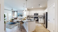 This thoughtfully designed one-bedroom, one-bathroom residence offers an efficient and functional layout across a single floor. The open-concept living and kitchen area serves as the heart of the home, where light wood-style flooring, recessed lighting, and high ceilings create a bright and airy atmosphere. The kitchen is equipped with stainless steel appliances, crisp white cabinetry, granite countertops, and a central island with seating — ideal for both meal preparation and casual dining. Pendant lighting above the island adds a stylish accent. The living room receives ample natural light through large windows and a glass door that opens to an outdoor area, further enhancing the sense of openness. The bedroom features a shiplap accent wall, a ceiling fan, and generous proportions, providing a comfortable retreat. A dedicated walk-in closet with built-in shelving and hanging rods offers practical storage. The bathroom includes a granite-topped vanity, wood-style flooring, and a shower-tub combination. A separate in-unit laundry room with a full-size washer and dryer adds everyday convenience. The cohesive, neutral color palette and coastal-inspired design elements give the space a clean, welcoming character throughout.