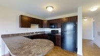 Located on Farmshed Road in Palmyra, Pennsylvania, this single-floor residence offers a functional and cohesive living environment. The kitchen serves as a standout feature, showcasing rich, dark wood cabinetry that extends to the ceiling for ample storage. Granite-style countertops in warm earth tones complement the cabinetry, while a curved breakfast bar adds a stylish and practical element for casual dining or food preparation. The kitchen is fully equipped with a full suite of black appliances, including a refrigerator, range with oven, and over-the-range microwave. A sink is conveniently positioned beneath the cabinetry along the side wall. Light hardwood flooring runs throughout, adding warmth and continuity to the space. Ceiling-mounted lighting provides consistent illumination throughout the kitchen area. The overall design palette — combining dark cabinetry, stone-inspired countertops, and warm flooring — creates a grounded, cohesive aesthetic throughout this single-story home in Lebanon County.