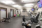 Located at 7171 Woodland Ave in West Des Moines, Iowa, this well-equipped fitness center offers a comprehensive workout environment within a efficiently utilized single-room layout. The space features durable speckled rubber flooring throughout, providing both safety and comfort during exercise. Overhead fluorescent lighting ensures the room is bright and well-illuminated at all times.

The cardio section is outfitted with multiple treadmills, an elliptical trainer, a stair climber, and a recumbent bike, catering to a variety of aerobic workout preferences. Multiple flat-screen televisions are mounted from the ceiling, allowing users to stay entertained during their sessions. A full-wall mirror along one side of the room enhances the sense of space and allows users to monitor their form.

The strength training area includes a dual-stack cable machine, a set of dumbbells on a tiered rack ranging across multiple weights, an adjustable workout bench, and a stability ball. Resistance bands and exercise mats are neatly organized on wall-mounted hooks. A water fountain and sanitation station with wipes are conveniently available to promote hygiene. The room is accented with dark wood trim and features the motivational phrase "YOUR ONLY LIMIT IS YOU" displayed prominently on the wall, setting an energizing tone for every workout.