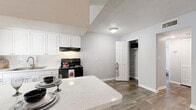 This single-story home at 5200 64th Circle East in Saint Petersburg, Florida offers a thoughtfully designed layout with a consistent, modern aesthetic throughout. Wood-look plank flooring runs across the living areas and bedrooms, providing a warm, cohesive feel underfoot. Textured ceilings and ceiling fans with integrated lighting are present in multiple rooms, contributing to comfort in Florida's climate.

The kitchen is a functional highlight, featuring white shaker-style cabinetry, a quartz-style countertop with a breakfast bar overhang, white tile backsplash, a black electric range with an overhead exhaust hood, and a dedicated pantry closet with built-in shelving. A window above the sink brings in natural light, and a skylight further brightens the space.

The living area is open and airy, with a large window fitted with blinds and direct access to the front entry. Bedrooms are well-proportioned, each equipped with ceiling fans, windows for natural light, and closet access — including one room featuring a dual-section walk-in style closet with wire shelving. The bathroom includes a full tub-shower combination with white tile surround and a window for ventilation. Clean, neutral gray walls carry throughout, creating a calm, move-in-ready environment.