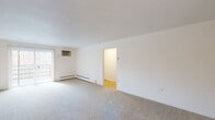 This single-floor residence offers a well-organized layout with distinct living, sleeping, and functional spaces. The generously sized living room is finished with neutral wall-to-wall carpeting and crisp white walls, creating a clean, versatile backdrop. A wall-mounted air conditioning unit and baseboard heating system provide year-round climate control, while a sliding glass door allows natural light to filter in and offers access to an outdoor area. The open feel of the living space is enhanced by a doorway connecting to the rest of the unit.

The kitchen stands out as a clear highlight, featuring rich wood cabinetry paired with deep granite countertops and a striking mosaic tile backsplash. Stainless steel appliances, including a dishwasher, complement the modern aesthetic, while a window above the sink brings in natural light and views of the surrounding landscape. Tile flooring completes the functional yet refined look.

Both bedrooms are carpeted and bathed in natural light through individual windows fitted with blinds. Each room is equipped with a ceiling fan and baseboard heating, ensuring comfort throughout the seasons. The bathroom is finished with warm beige tile surrounding a full tub and shower combination, accented by dark decorative tile details, a mirrored vanity, and a window for natural ventilation.